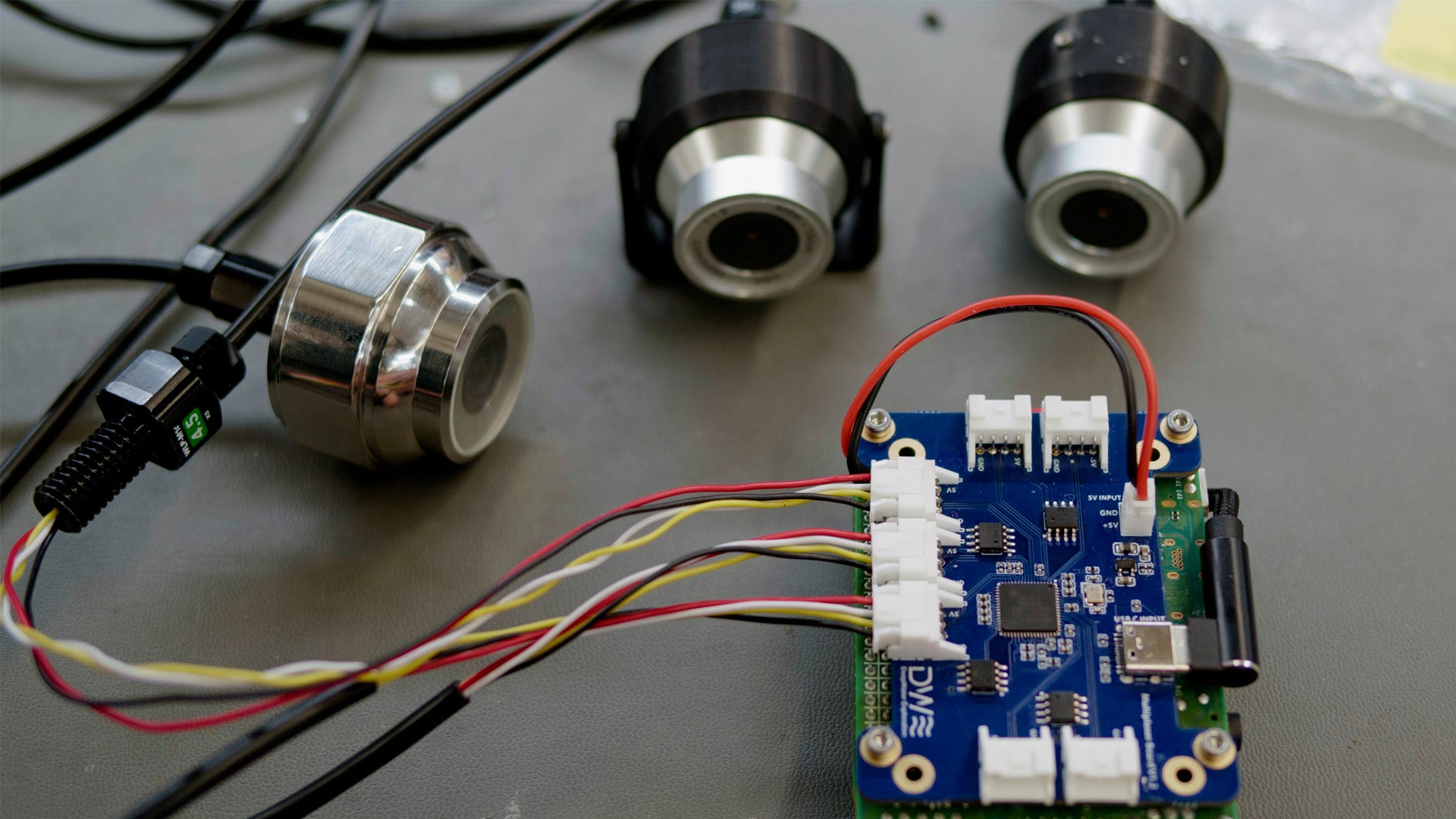 Three DeepWater Exploration exploreHD subsea cameras connected to a DWE 7-Port USB Multiplexer board, demonstrating a multi-camera configuration for ROV, AUV, or other underwater systems requiring multiple USB 2.0 device inputs via JST connectors.