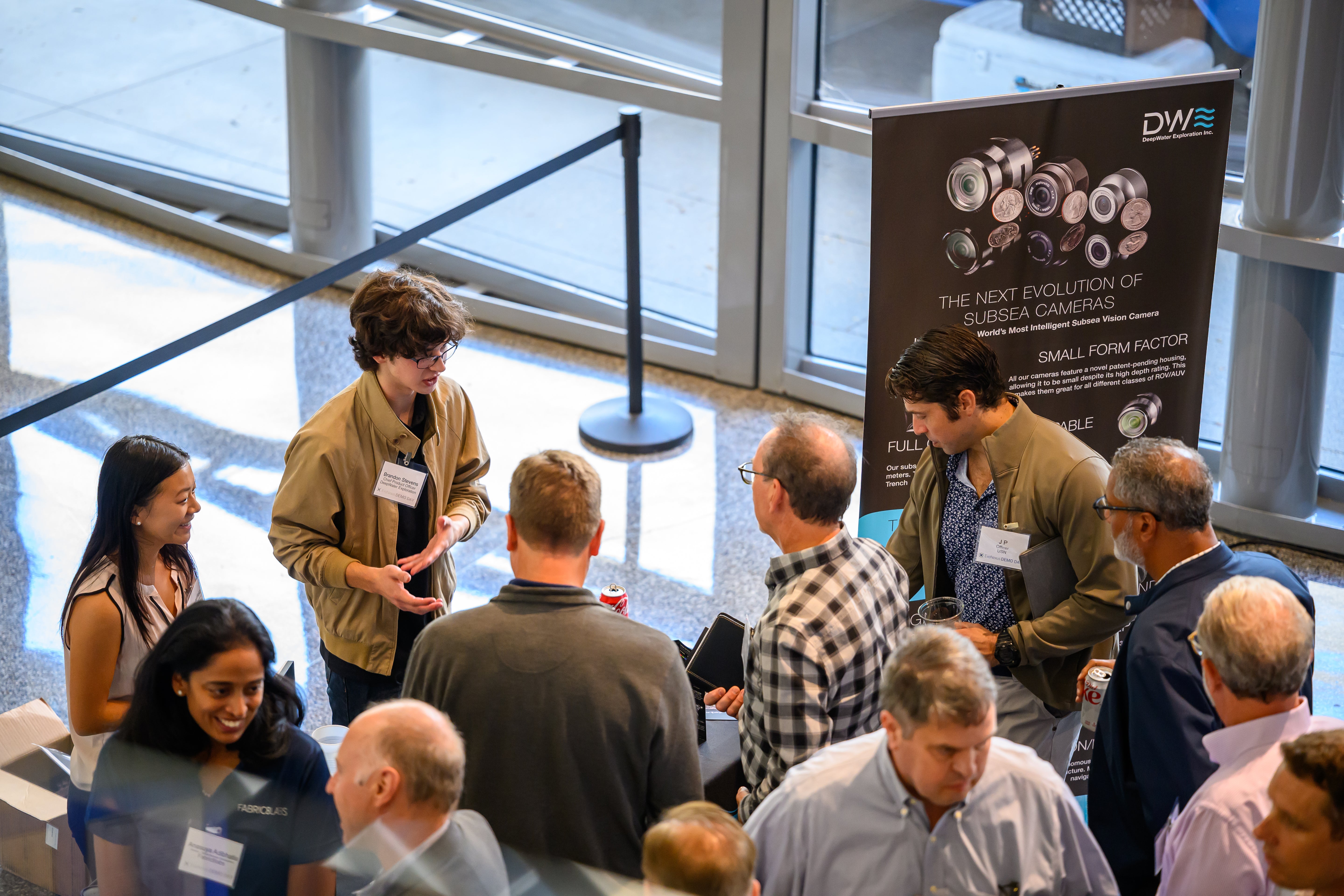 Attendees engage with representatives at a DWE subsea technology booth, discussing next-generation underwater cameras for ROVs, AUVs, ASVs, and marine robotics. The booth highlights compact, high-resolution subsea vision systems designed for industrial inspection, offshore energy, and ocean exploration.